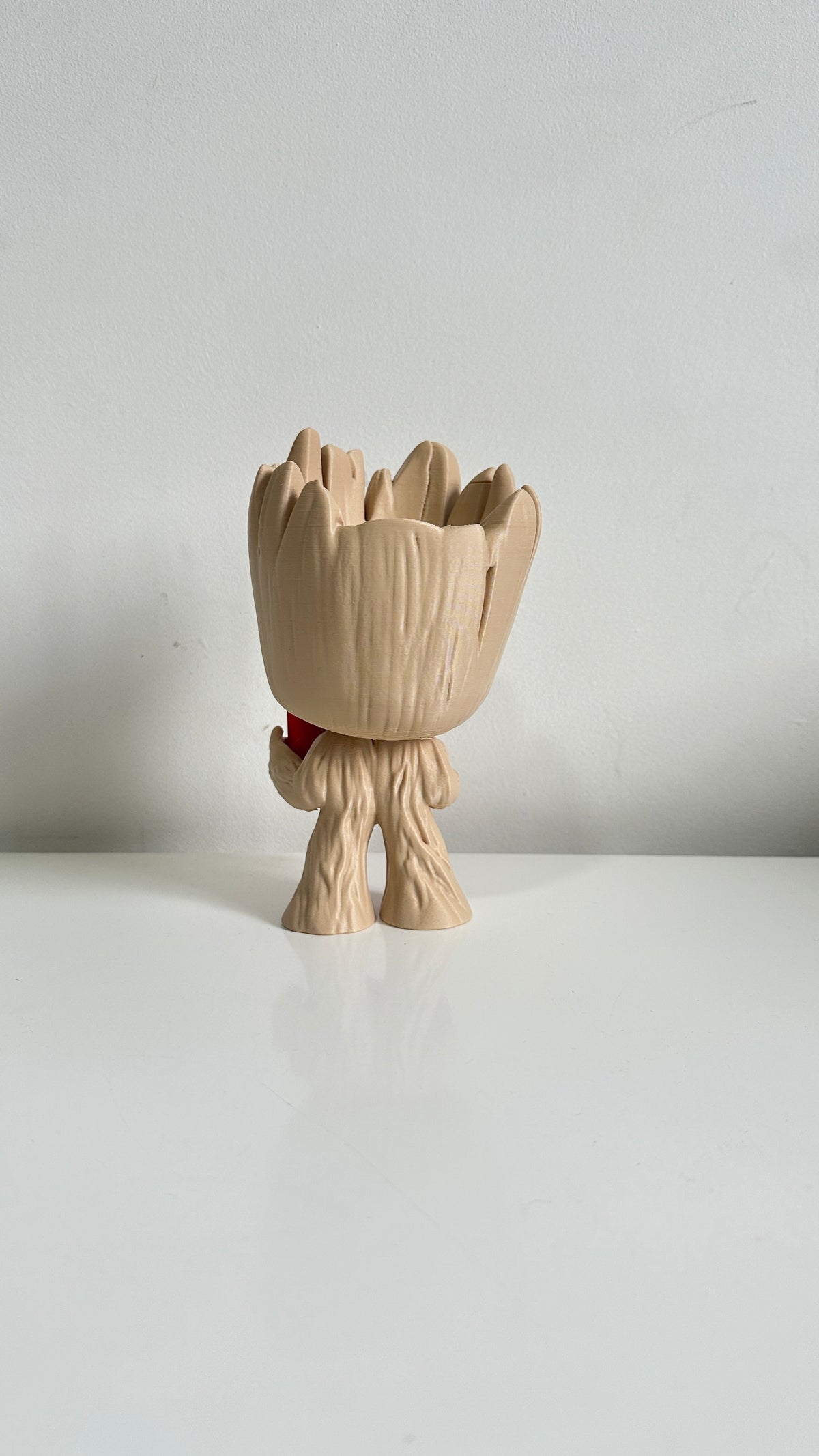 Figurine petit arbre beige tenant un cœur rouge, vue de trois quarts