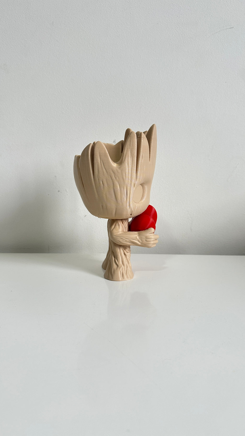 Figurine petit arbre beige tenant un cœur rouge, vue de profil