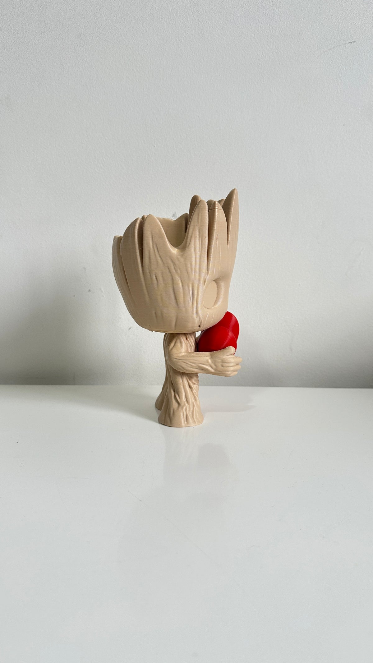 Figurine petit arbre beige tenant un cœur rouge, vue de profil