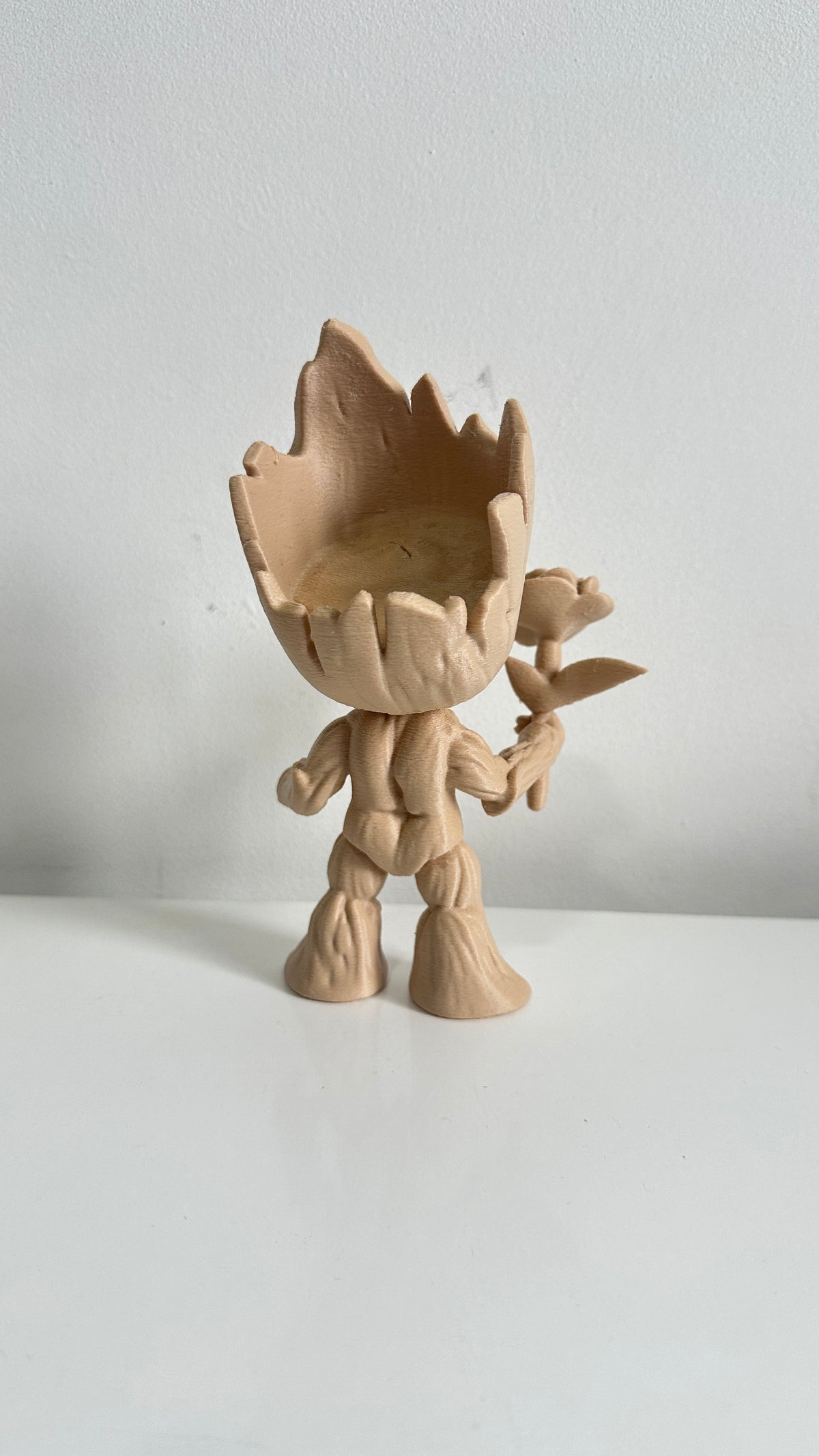 Figurine petit arbre beige tenant une fleur, vue de trois quarts