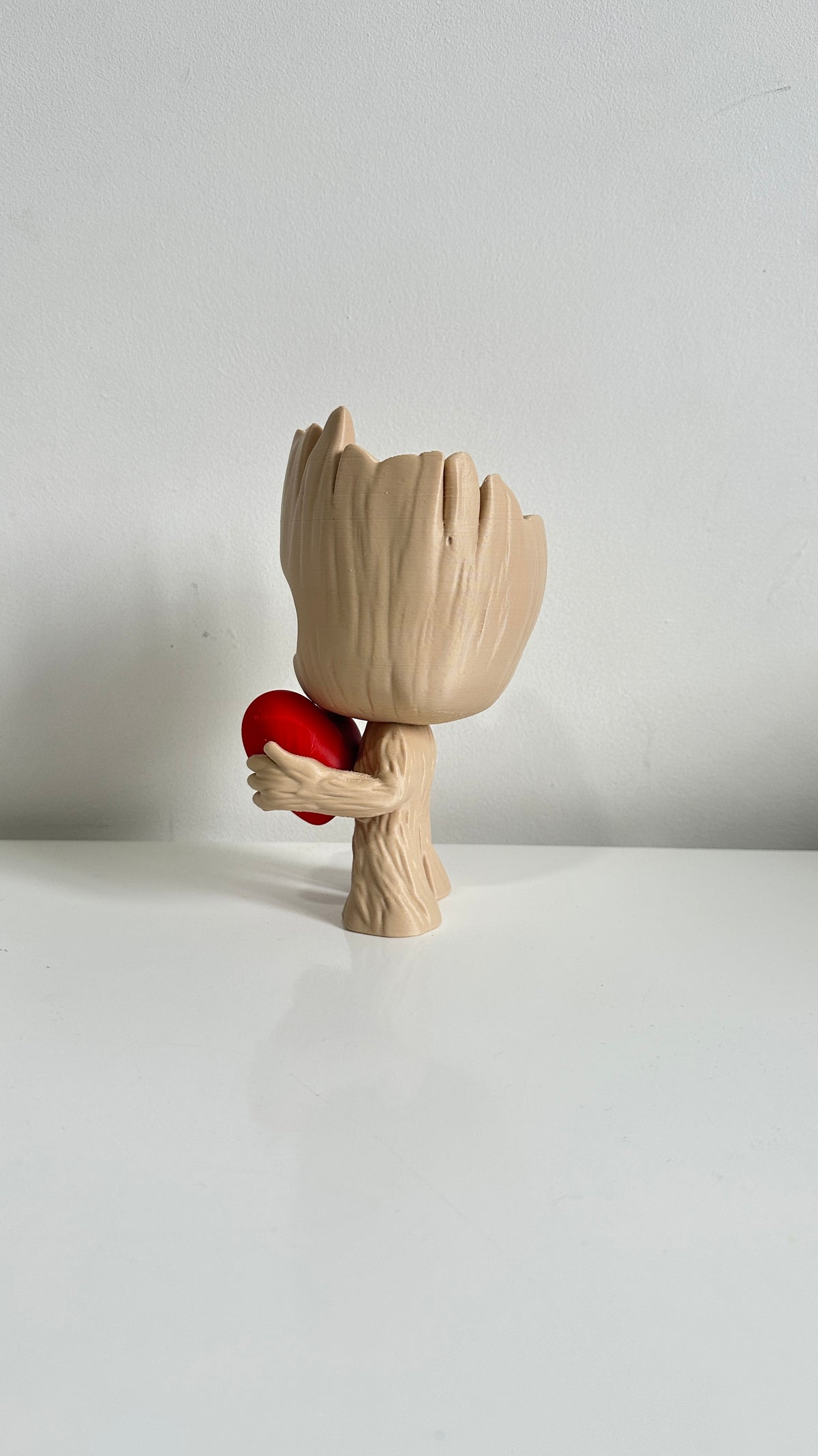 Figurine petit arbre beige tenant un cœur rouge, vue de dos