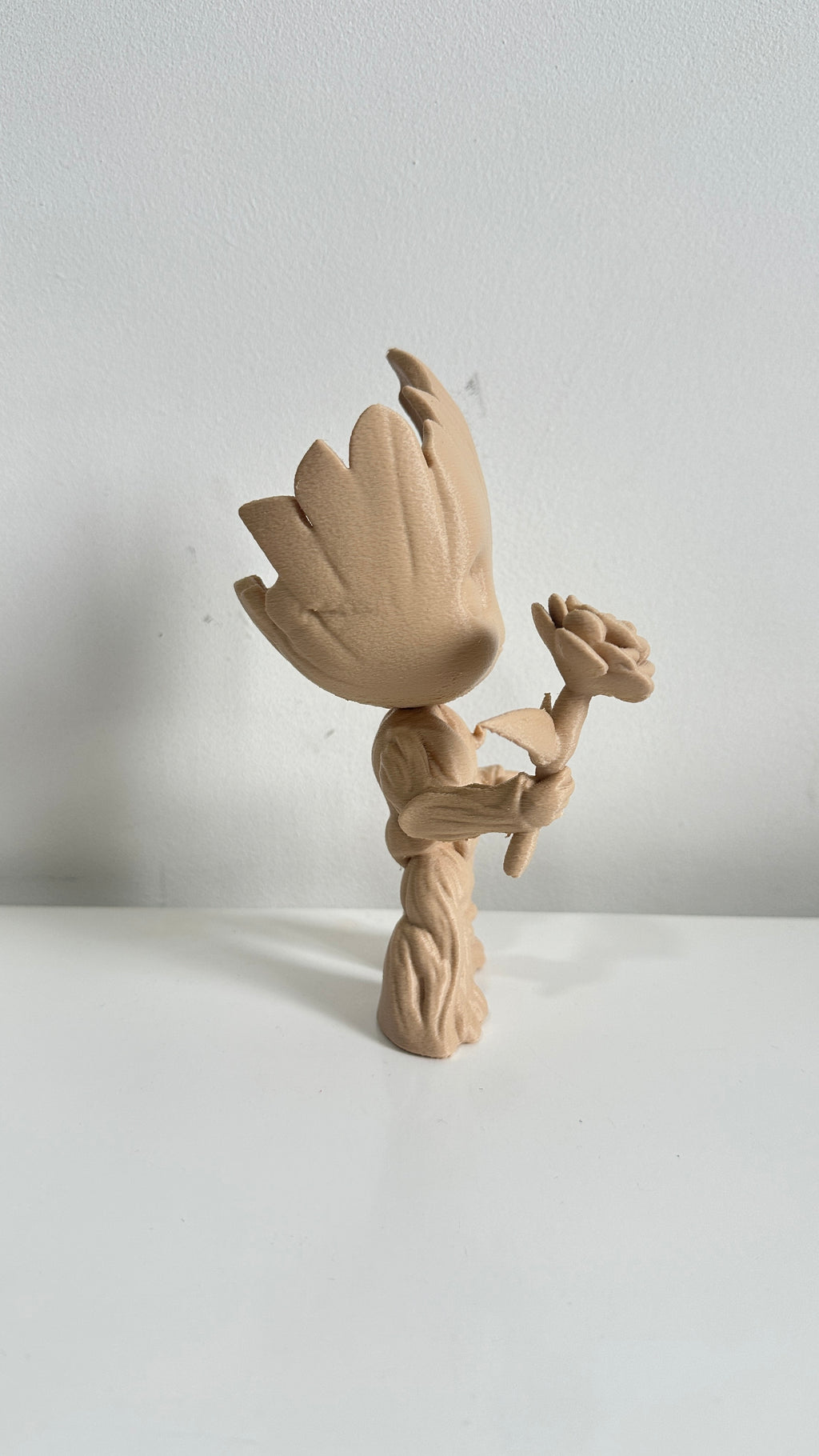 Figurine petit arbre beige tenant une fleur, vue de dos