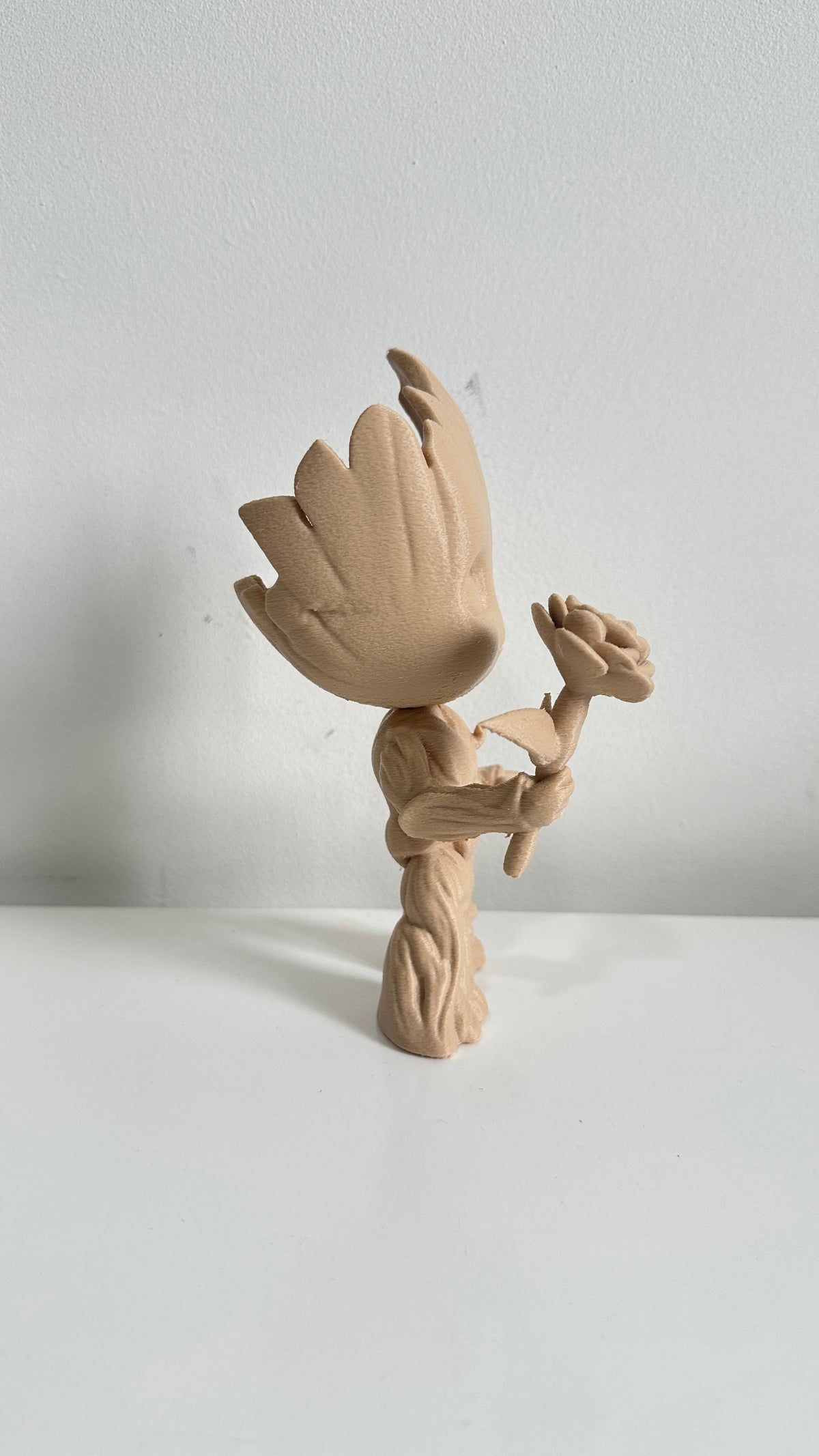 Figurine petit arbre beige tenant une fleur, vue de dos