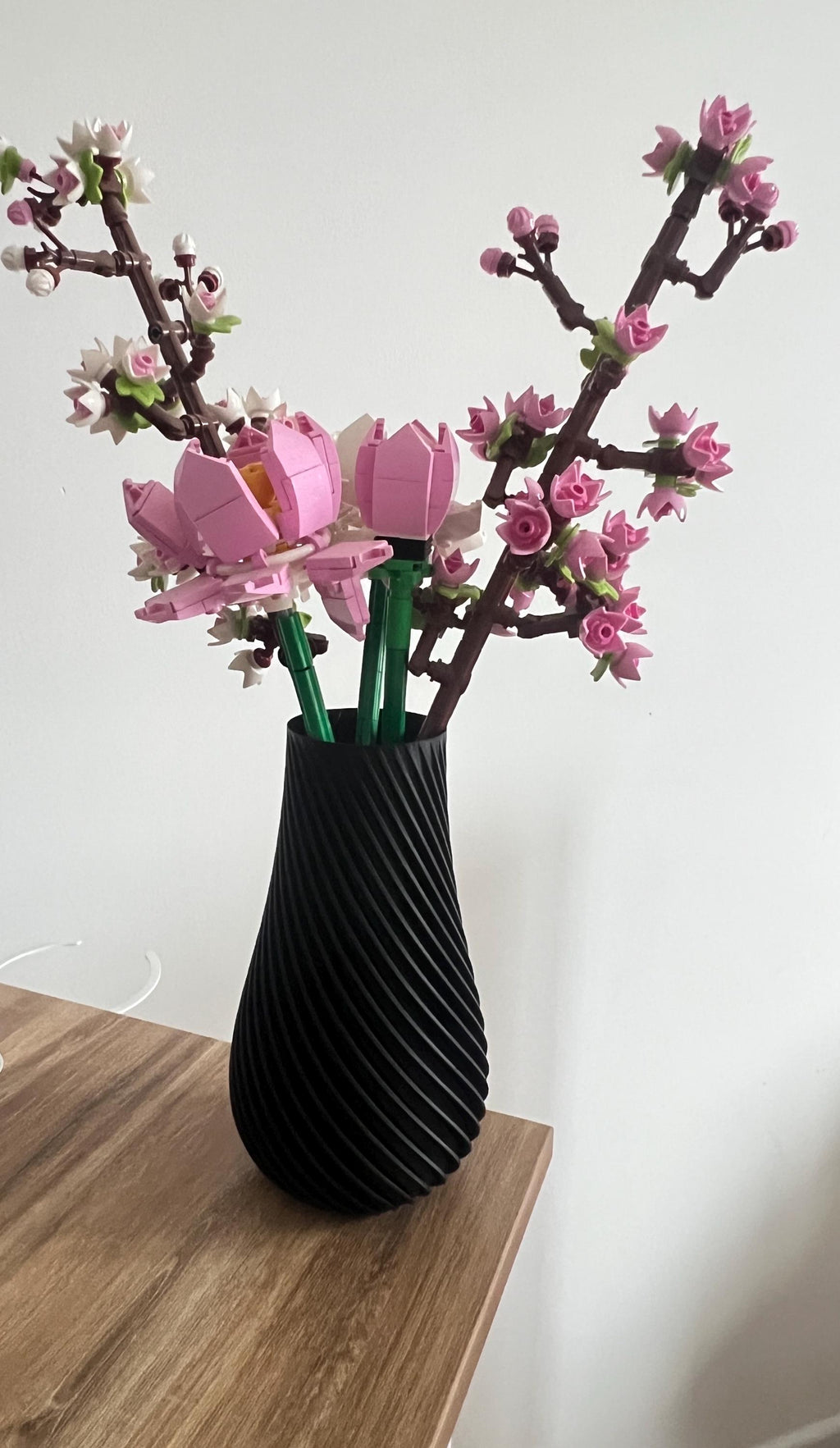 Vase torsadé noir avec fleurs de cerisier LEGO® sur un meuble en bois